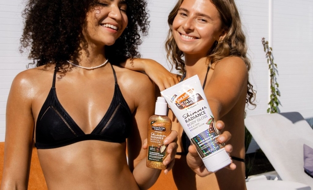 Two smiling women in bikinis proudly display their Palmer's Shimmer Radiance Body Oil and Shimmer Radiance Body Gloss , excited for a sunny day by the pool together.